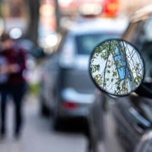 close-up of a motorcycle mirror parked on the side of the street, soft focus, blurred background